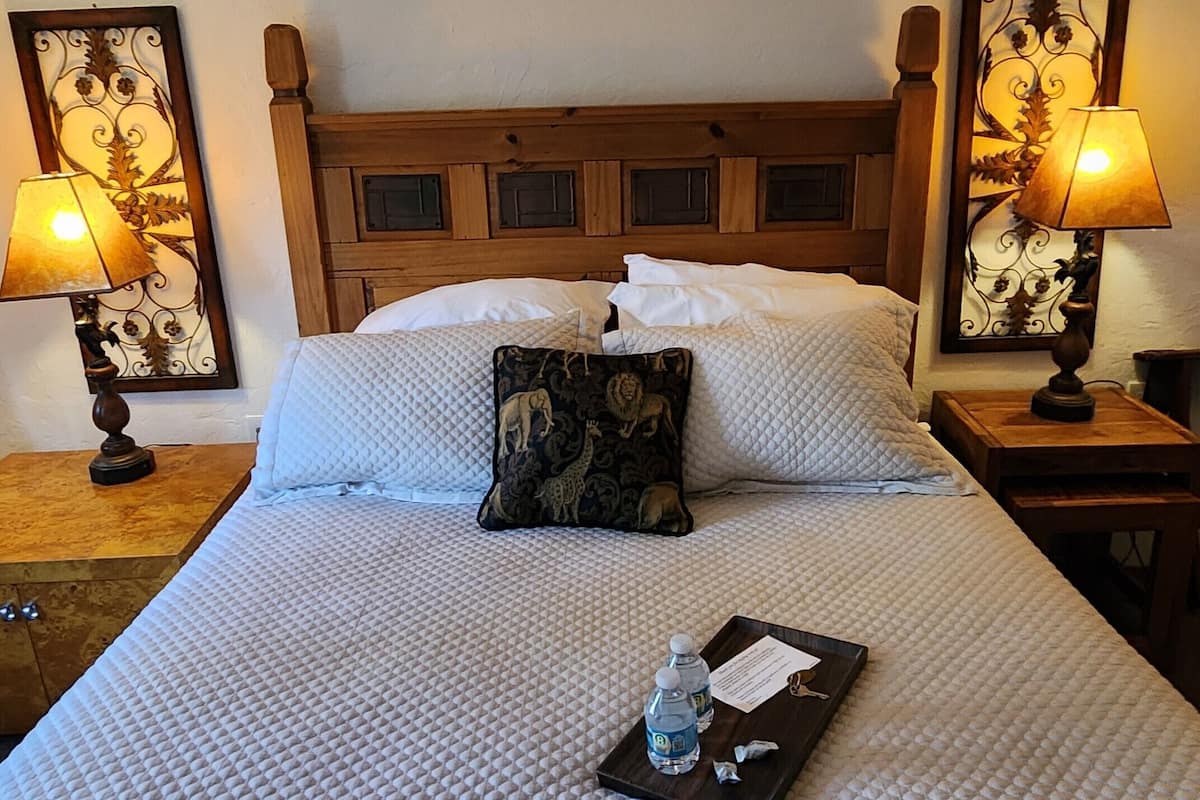 A neatly made bed with a quilted cover, two pillows, a decorative pillow, and a tray with a water bottle and keys.