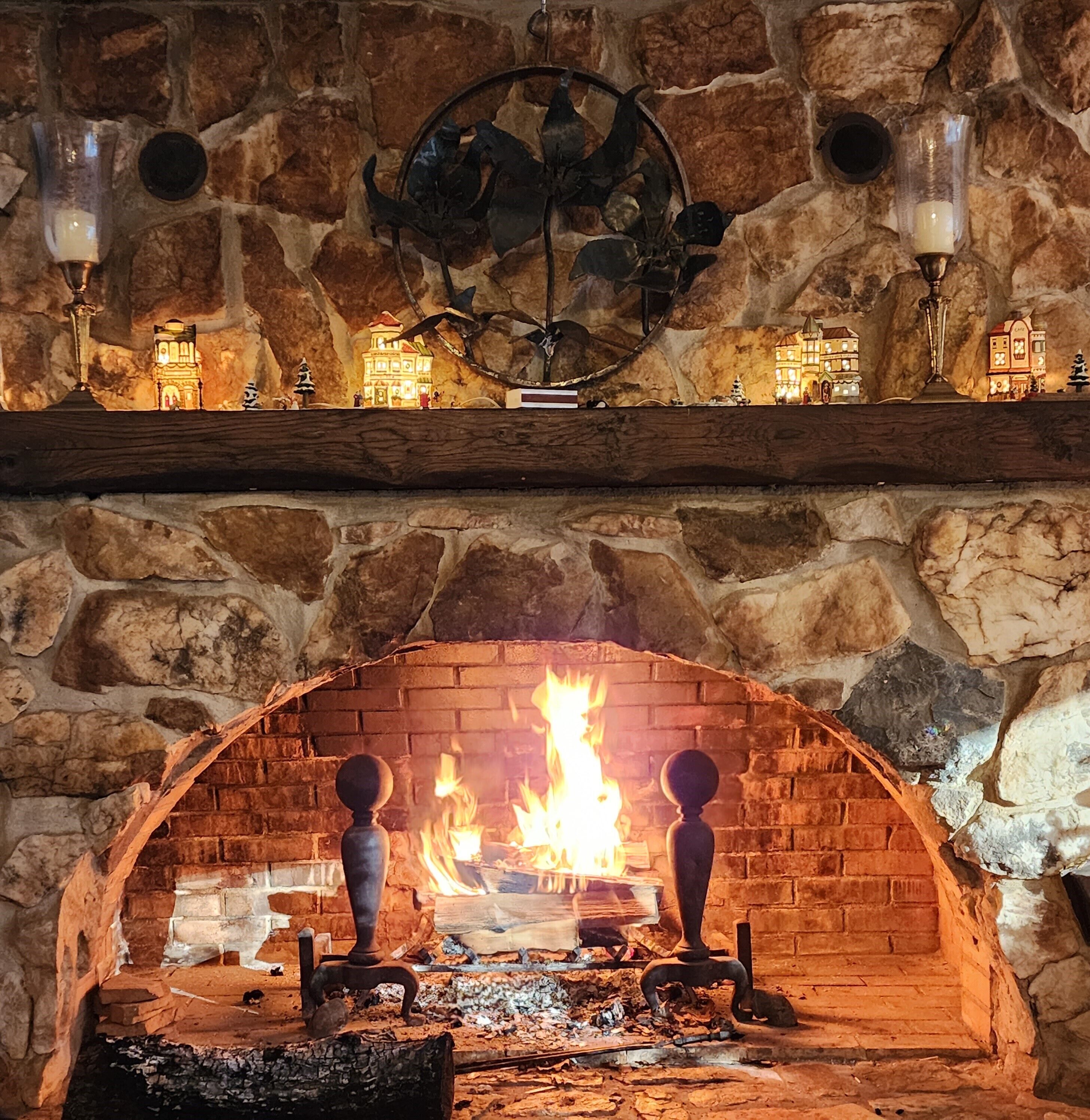 A stone fireplace with a fire, a wooden mantel with small figurines, and two wall-mounted sconces.