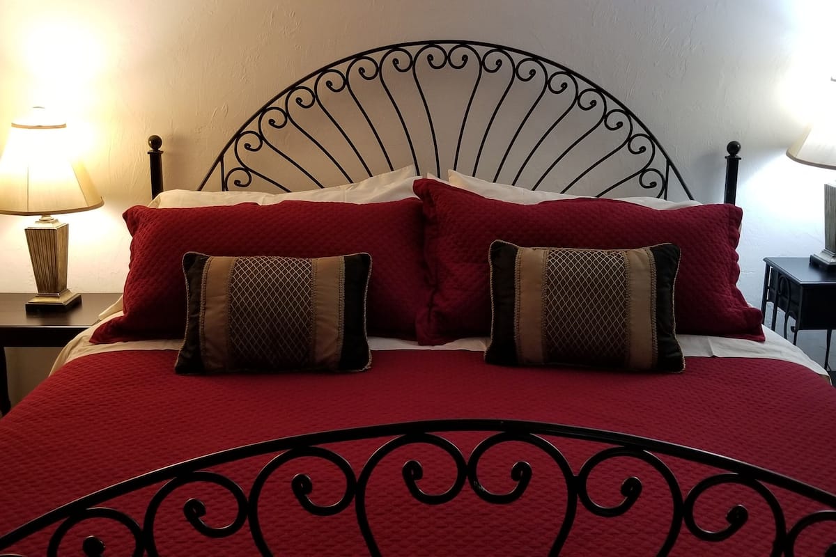 A neatly made bed with a red bedspread and two decorative pillows, flanked by two bedside tables with lamps.