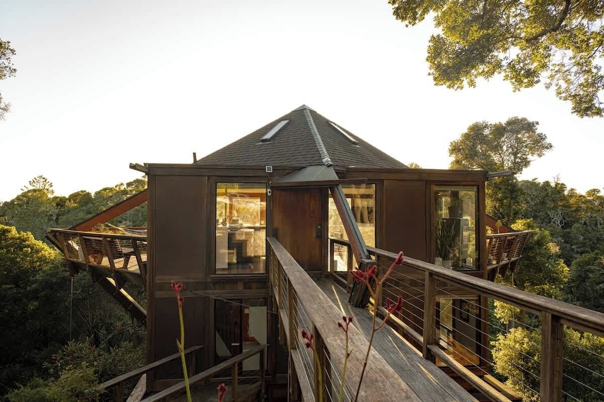 A modern house with a wooden deck, large windows, and a view of the surrounding forest.