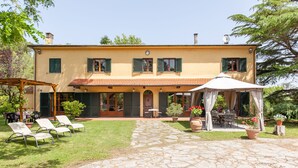 Una casa de dos plantas con un patio, mobiliario exterior y un espacio de estar cubierto.