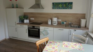 Una cocina con armarios blancos, estufa, fregadero y un cuadro en la pared.
