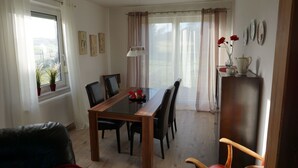 Un comedor con una mesa de vidrio, sillas, un radiador, una ventana con cortinas y vistas al exterior.