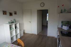 Ein Zimmer mit Holzboden, weißen Wänden, einem Esstisch mit Stühlen sowie einer Küchenzeile mit Toaster und einer Tür zu einem weiteren Raum.
