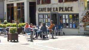 Un café con mesas al aire libre y un escaparate con un cartel que dice "CAFE DE LA PLACE".