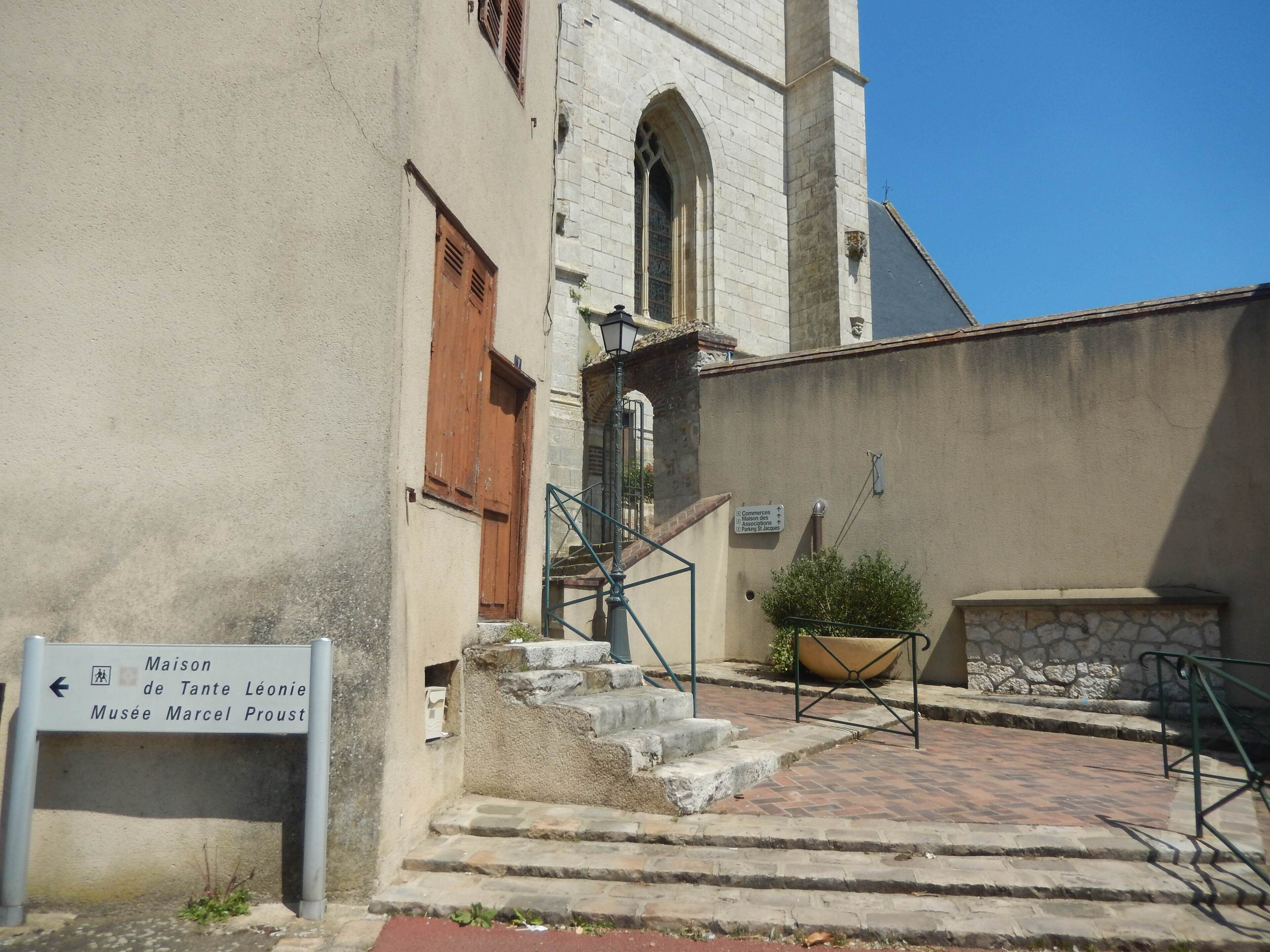 Ein Gebäude mit einer Steinfassade, einer Holztür und einem Schild, das Hinweise zu 'Maison de Tante Léonie' und 'Musée Marcel Proust' gibt.