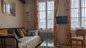 Una habitación con cama, una mesa de vidrio, una silla, un televisor y una ventana con cortinas.