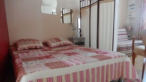 Un dormitorio con cama, mesita de noche, una silla y una ventana con cortinas.