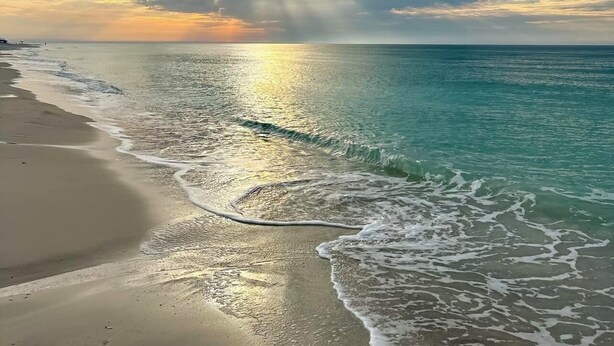 Una playa con agua cristalina y un atardecer.