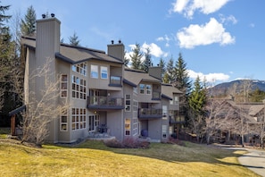 A multi-story house with a balcony, a chimney, and a view of trees and mountains.