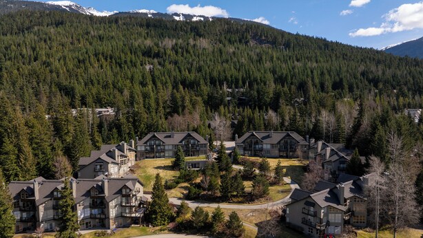A residential area with multiple two-story houses, surrounded by dense forest and mountains in the background. - Blackcomb Greens by Whistler Premier (Whistler)