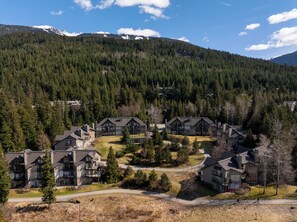 A residential area with multiple two-story houses, surrounded by dense forest and mountains in the background. - Blackcomb Greens by Whistler Premier (Whistler)
