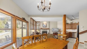 A dining area with a wooden table and chairs, a chandelier, and a stone fireplace. - Blackcomb Greens by Whistler Premier (Whistler)