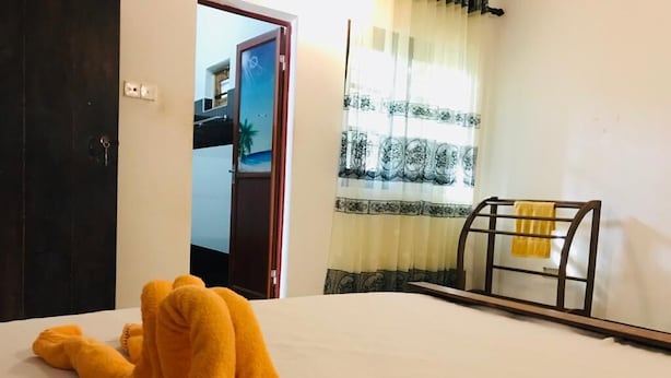 A room with a bed, a window with patterned curtains, and a door leading to another room. - Asha Villa Weligama (Weligama)