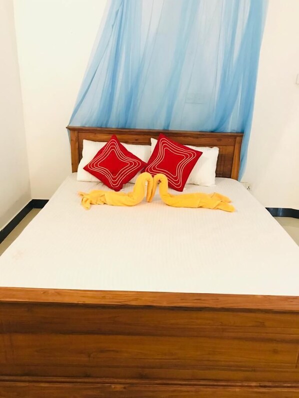 A bed with a wooden headboard, two red pillows, and a yellow towel. - Asha Villa Weligama (Weligama)