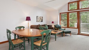 A dining area with a wooden table and chairs, a sofa, and a window with a view of trees. - Tree Line by Whistler Premier (Whistler)