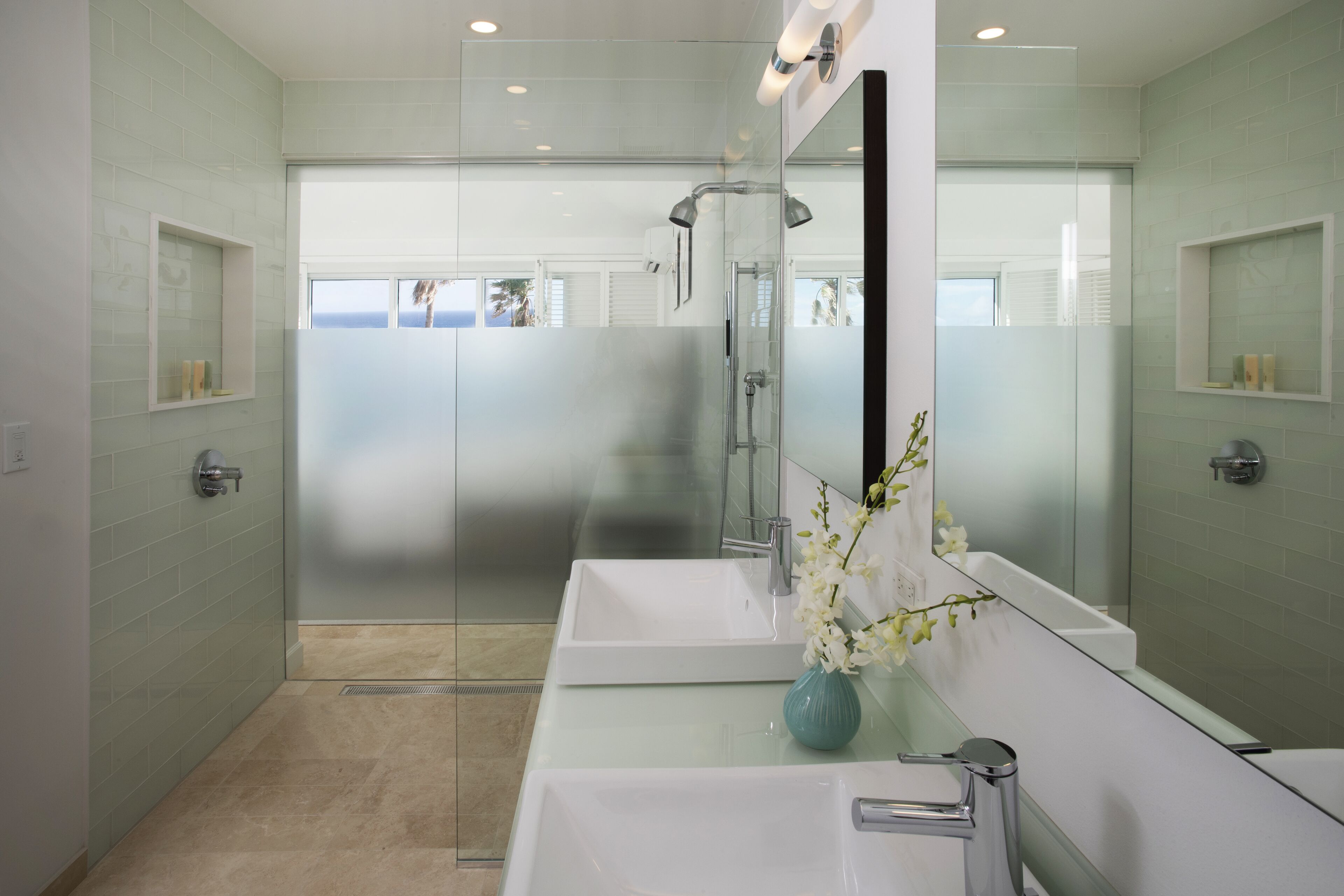 A modern bathroom with two sinks, a large mirror, and a glass shower enclosure.