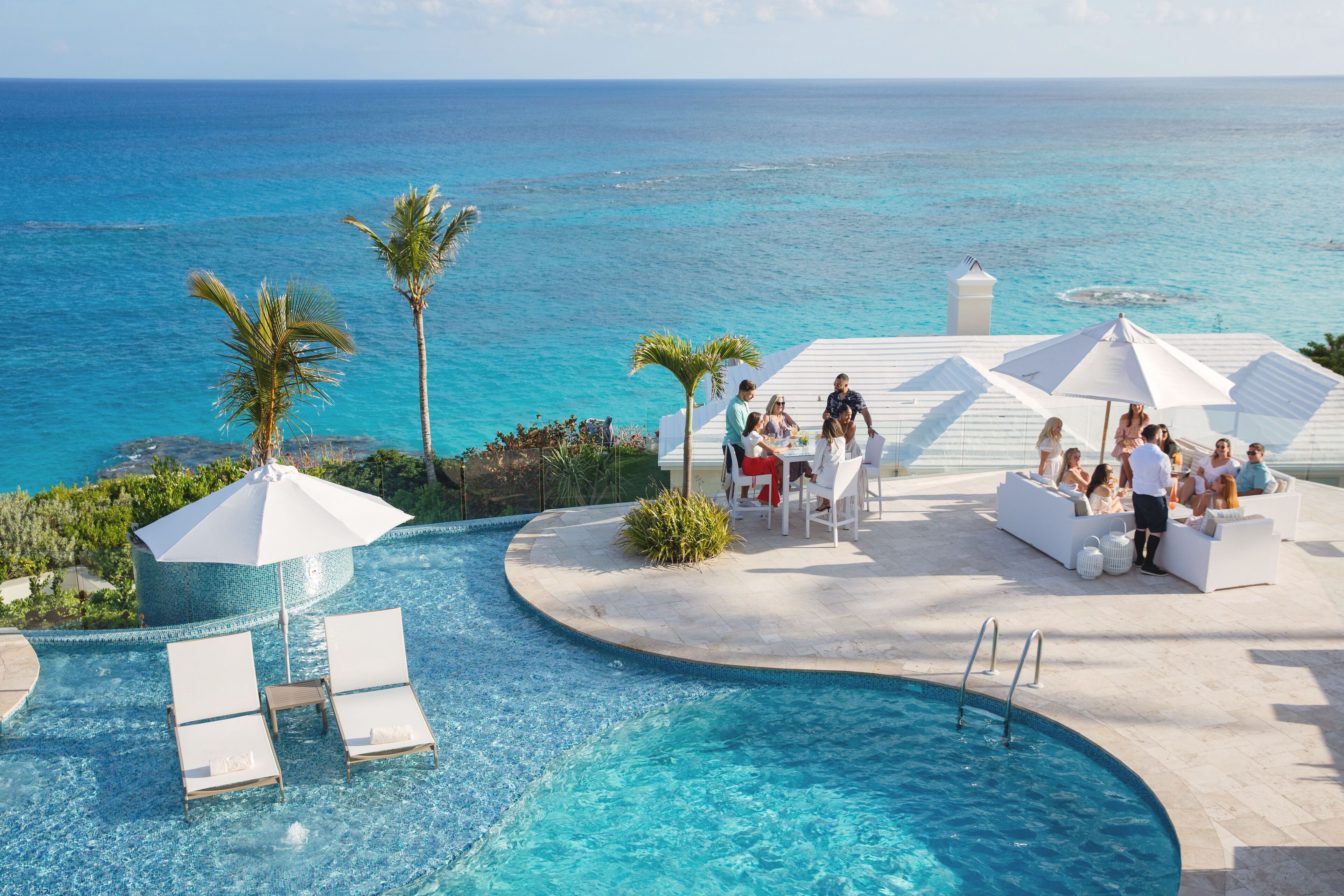 A pool area with lounge chairs and umbrellas, overlooking a clear blue ocean.