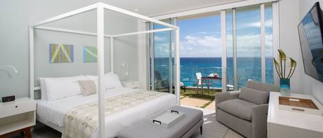 Un dormitorio moderno con una cama con dosel, un sofá gris y un balcón con vistas al océano.
