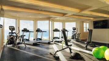 Un gimnasio con cintas de correr, elípticas y pelotas de ejercicio, con amplias ventanas que ofrecen vistas al mar.