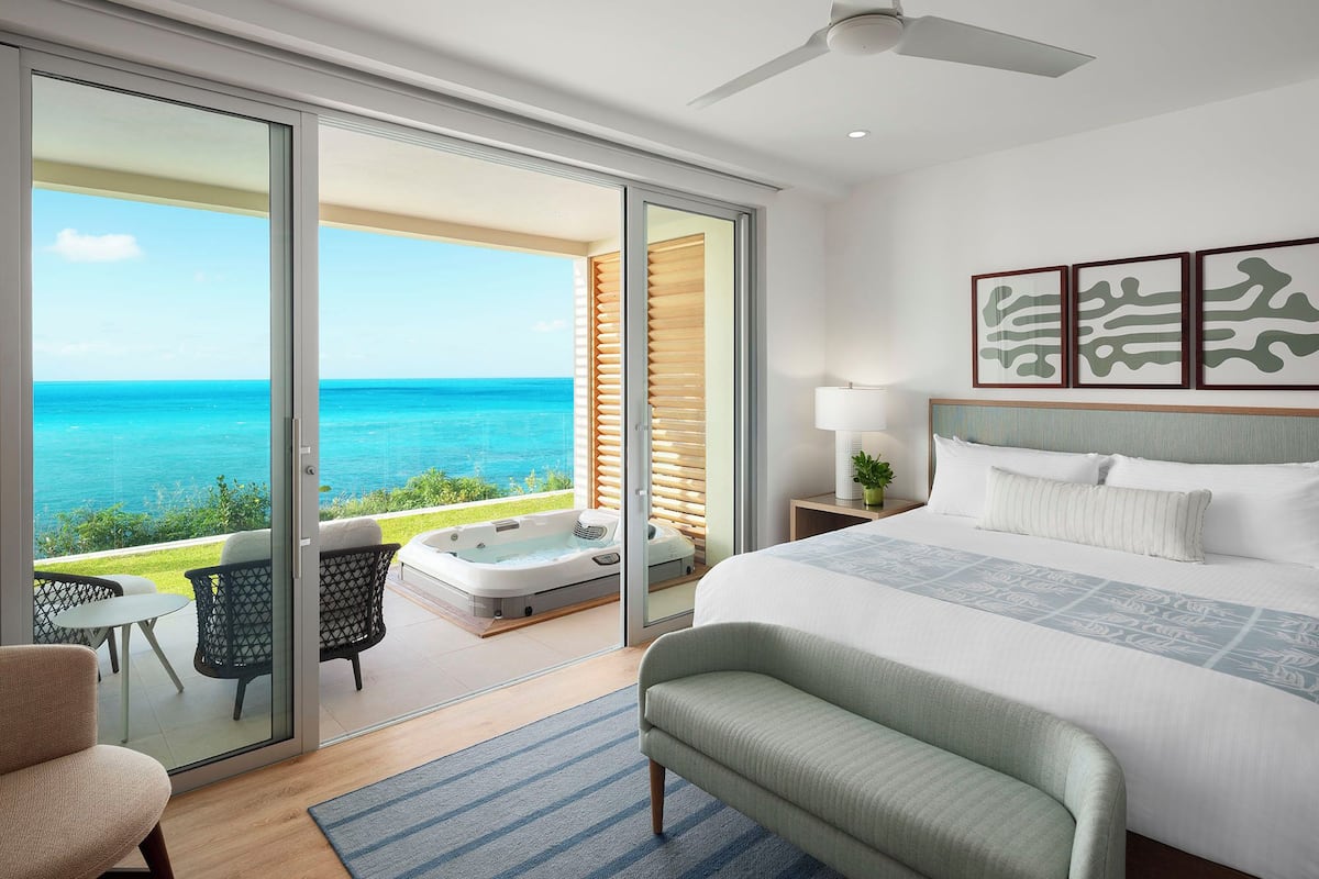 Um quarto espaçoso com uma cama grande, um ventilador de teto e vista para o oceano através de portas de correr.