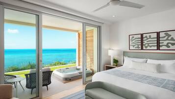 A spacious bedroom with a large bed, a ceiling fan, and a view of the ocean through sliding glass doors.