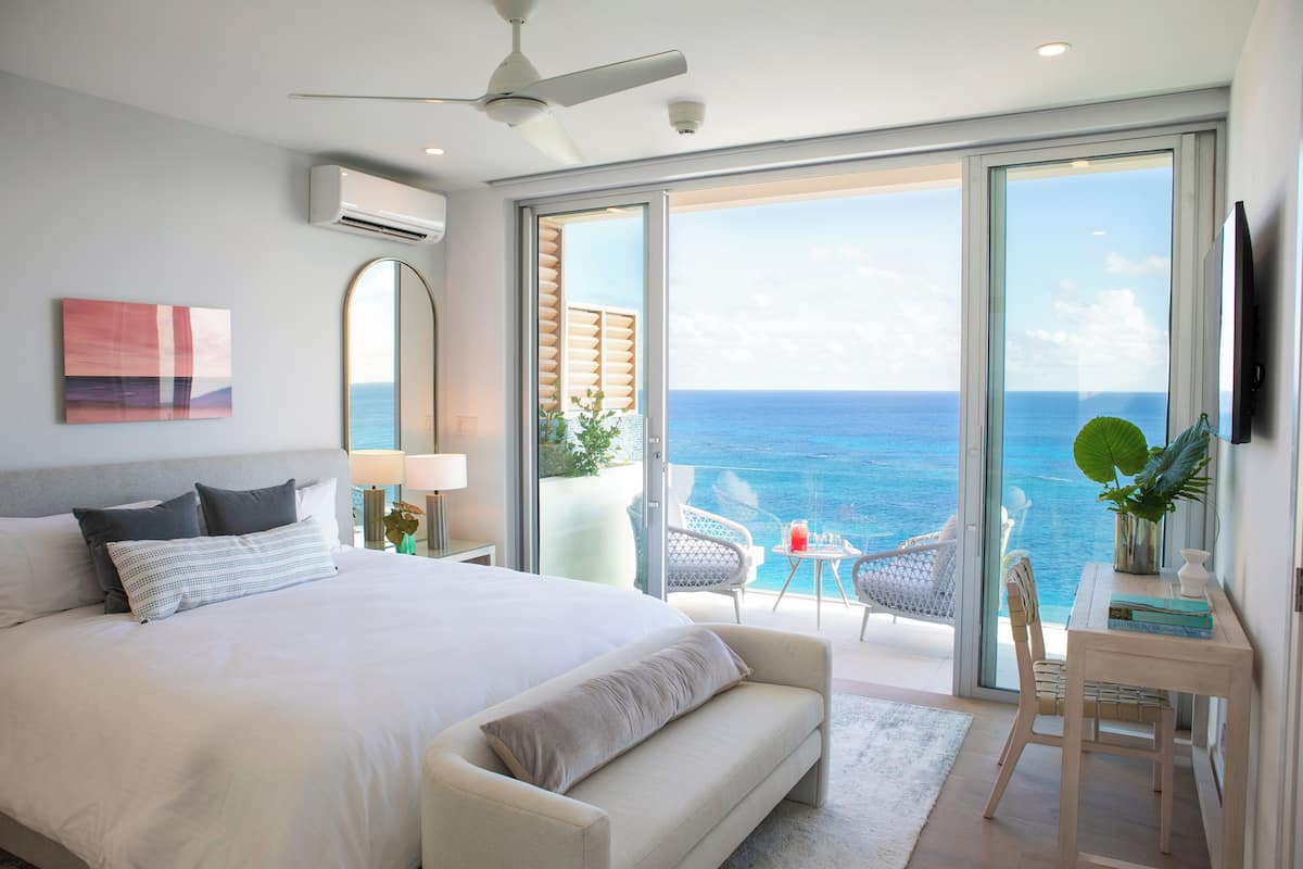 Ein modernes Schlafzimmer mit einem großen Bett, einem Deckenventilator und Meerblick durch große Schiebetüren.