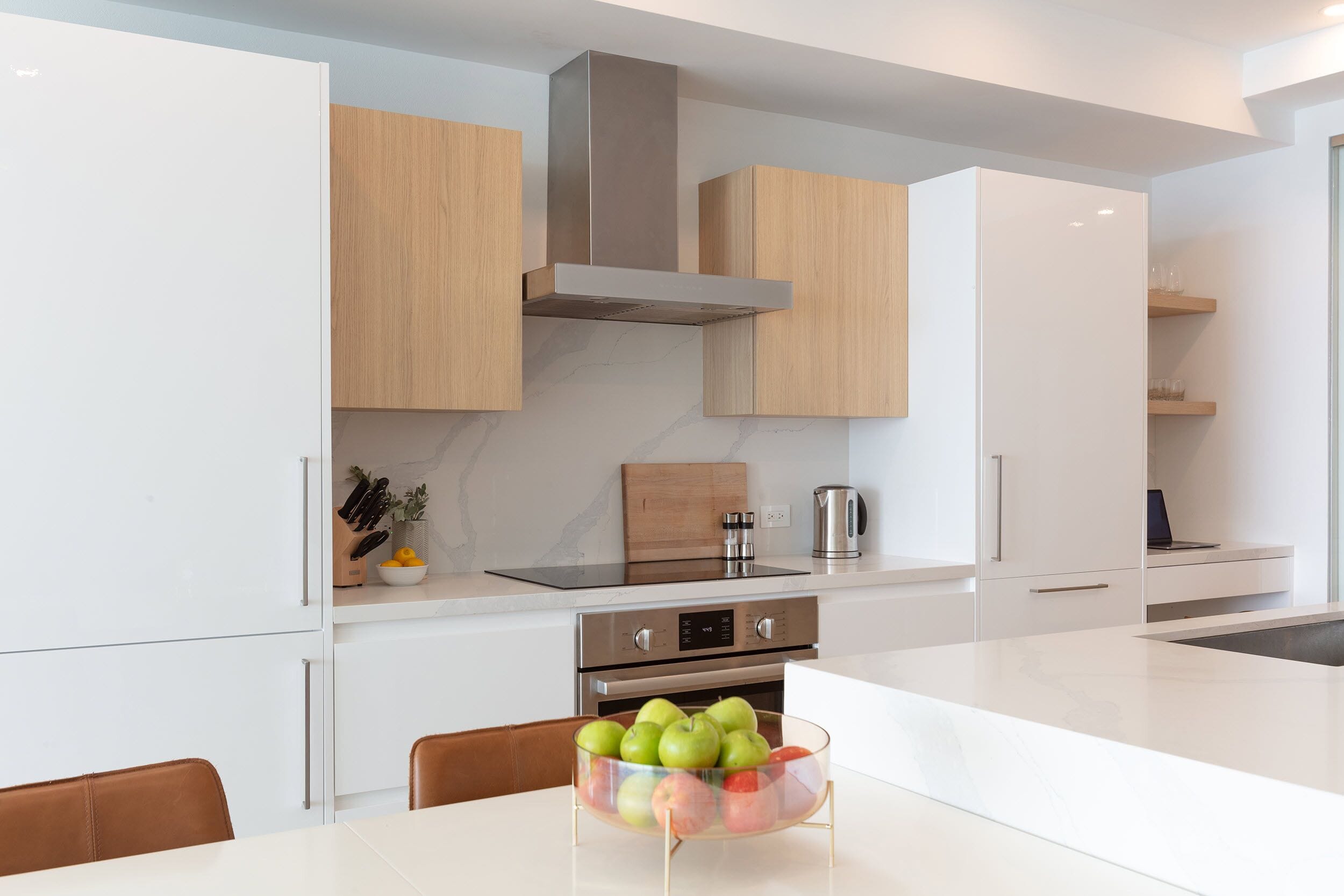 A modern kitchen with white cabinets, a stainless steel range, and a central island with a bowl of apples.