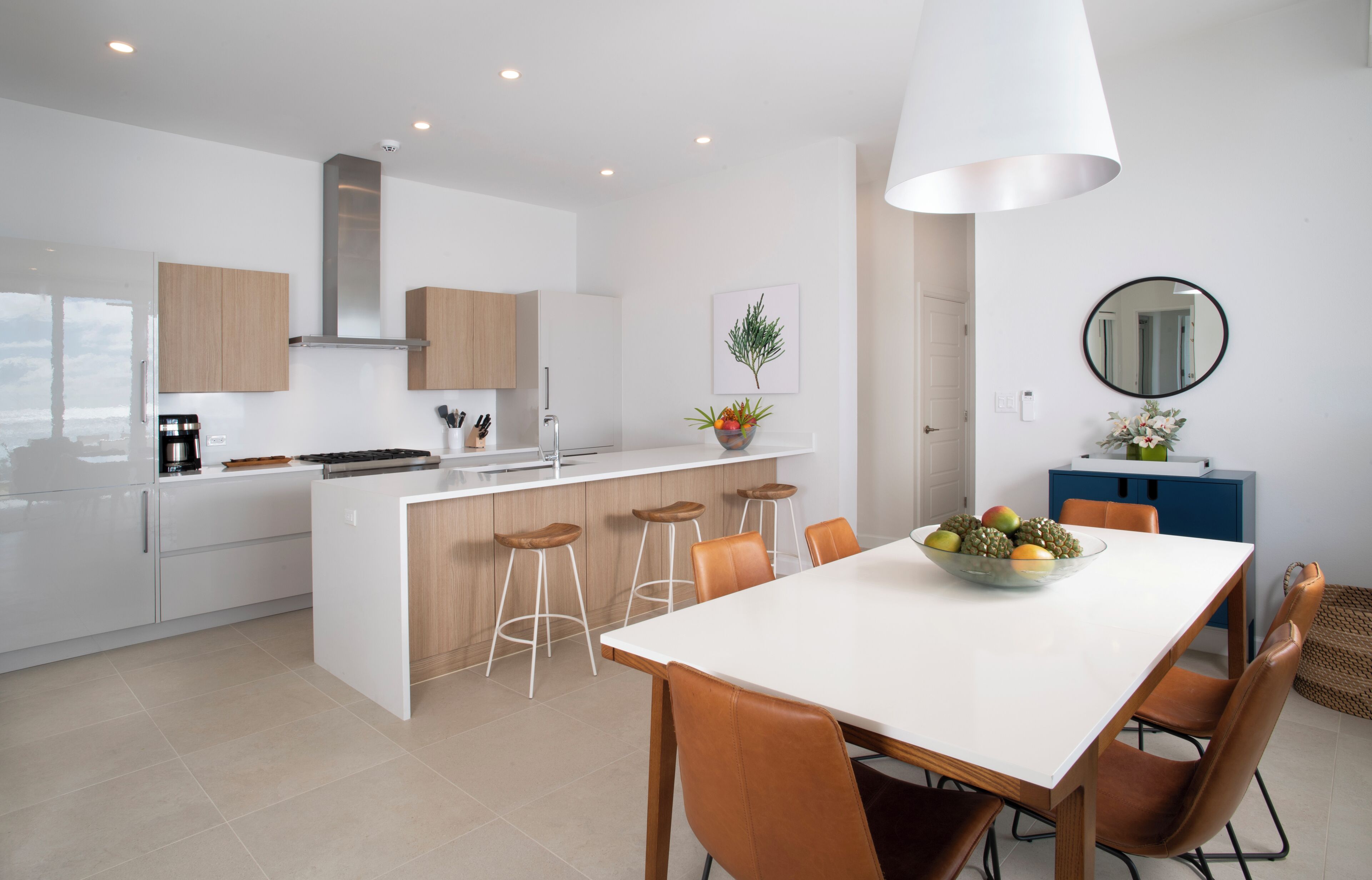 A modern kitchen with white cabinets, a central island with stools, and a dining area with a white table and brown chairs.