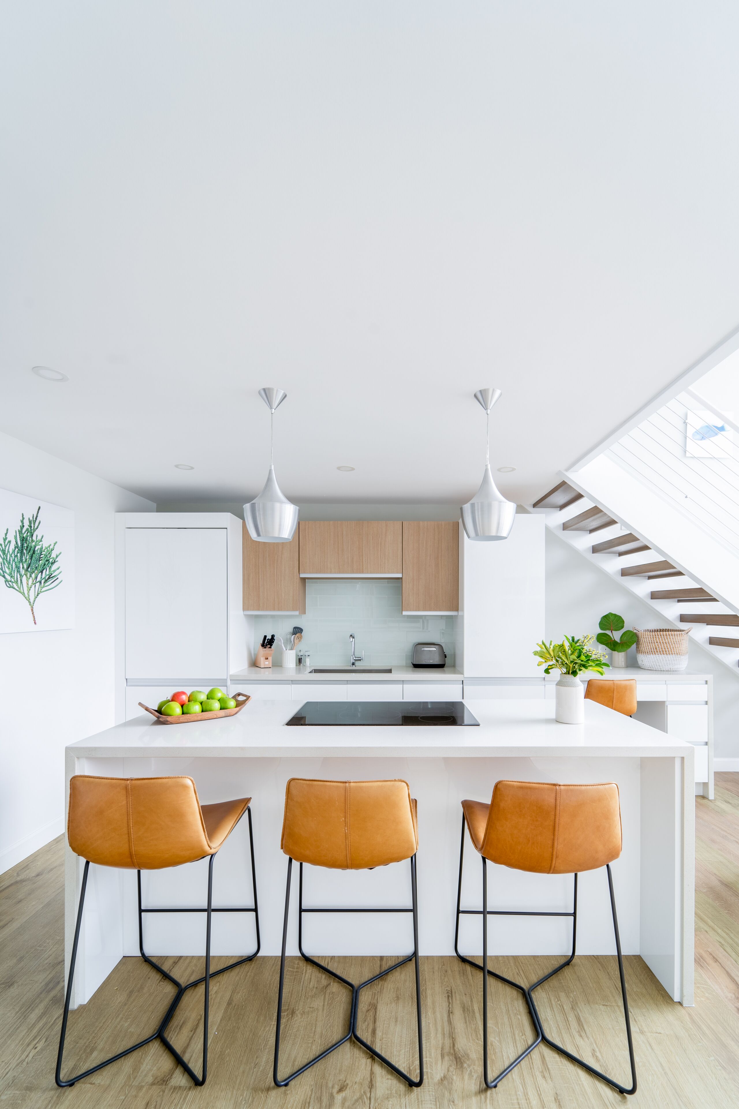 A modern kitchen with a central island, three bar stools, pendant lights, and wooden cabinets.