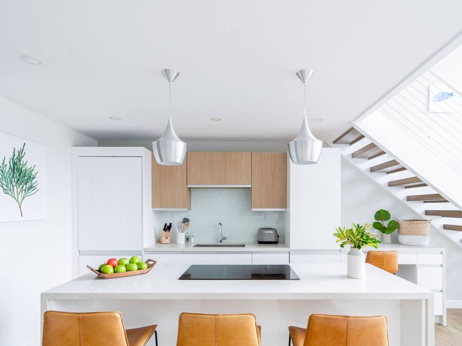 A modern kitchen with a central island, three bar stools, pendant lights, and wooden cabinets.