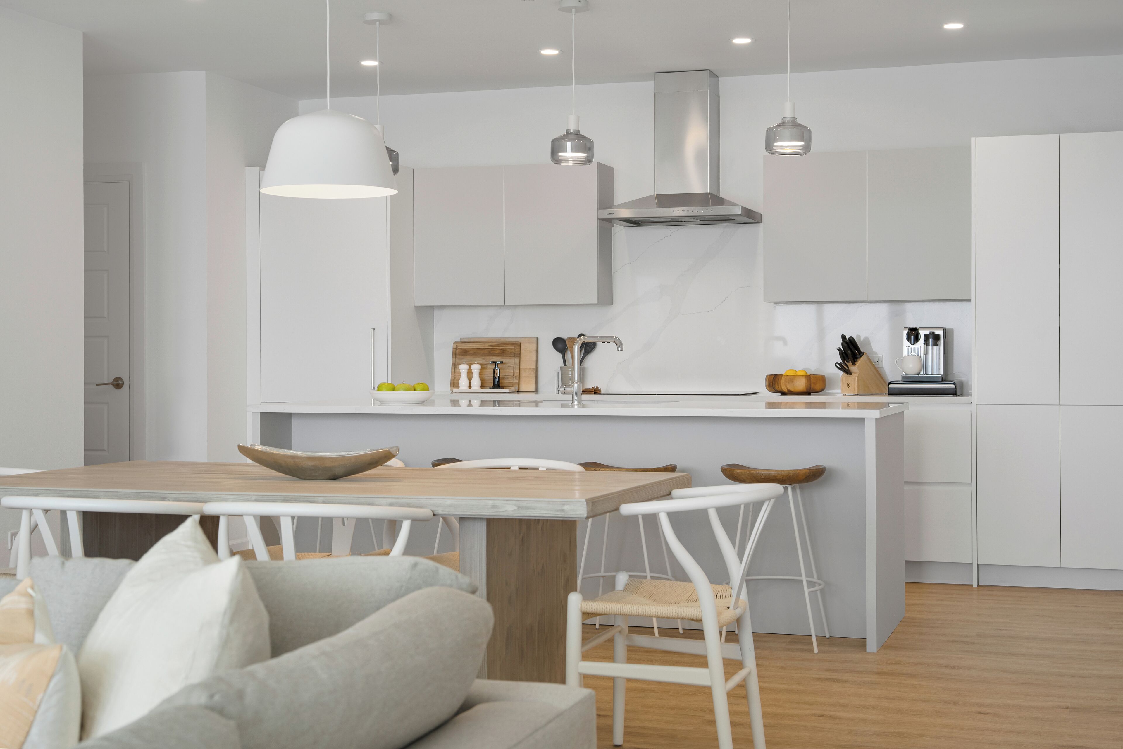 A modern kitchen with white cabinetry, a wooden island, pendant lighting, and a dining area with a table and chairs.