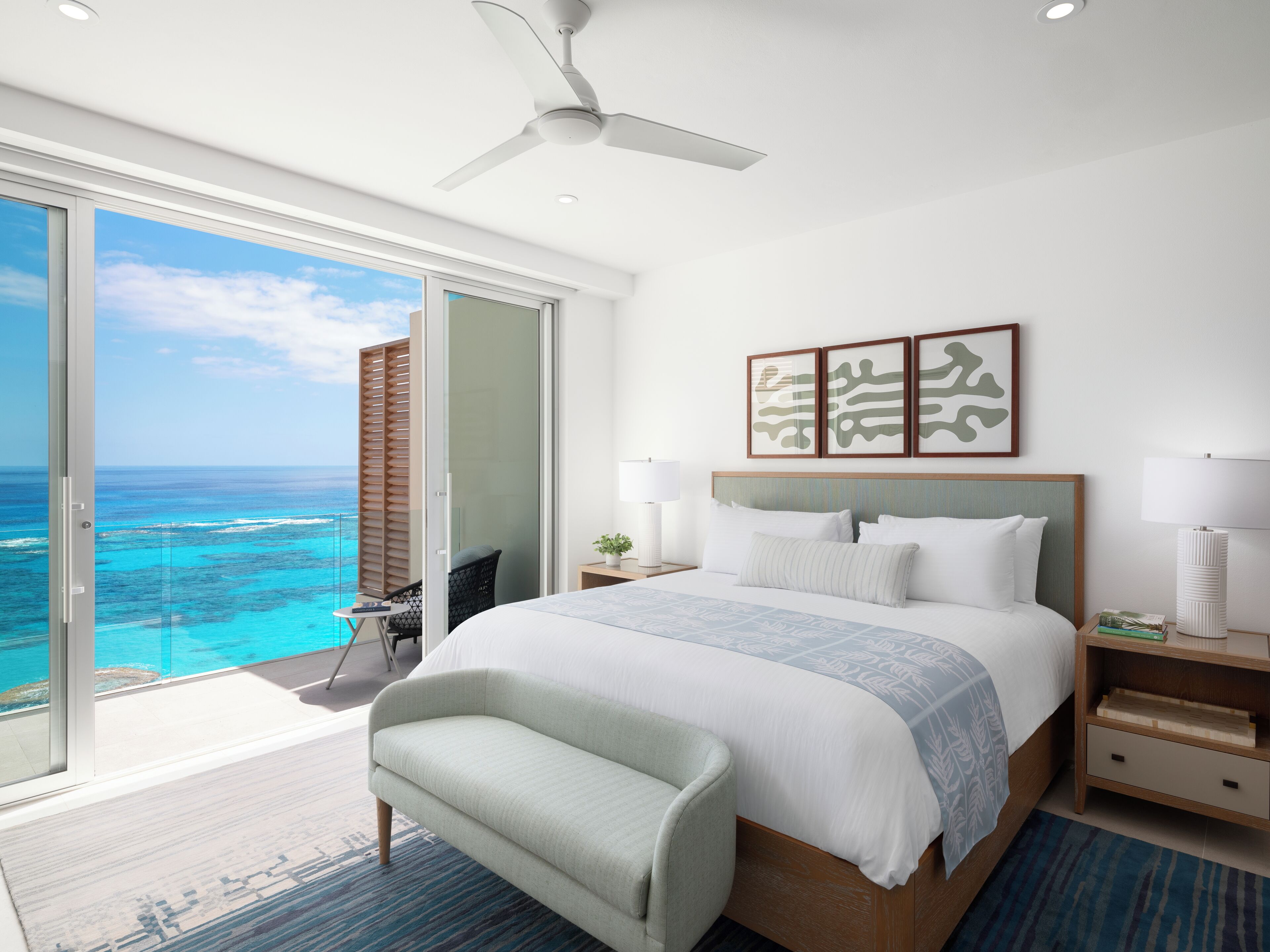 A modern hotel room with a large bed, a ceiling fan, and a view of the ocean.