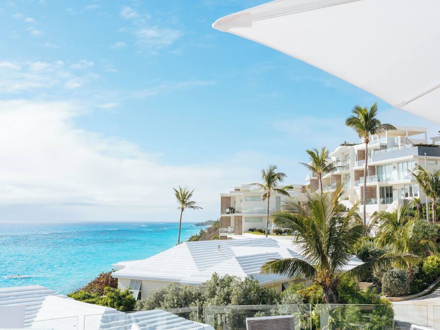 A coastal hotel with white buildings, palm trees, and a view of the ocean.