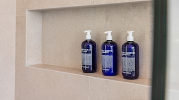 Three bottles of SUN+GOETZ body wash on a beige tiled shelf.