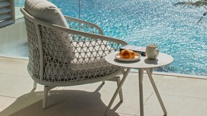 Un balcon avec un fauteuil en osier blanc, une petite table ronde sur laquelle se trouvent une assiette de nourriture et une tasse, donnant sur un océan scintillant.