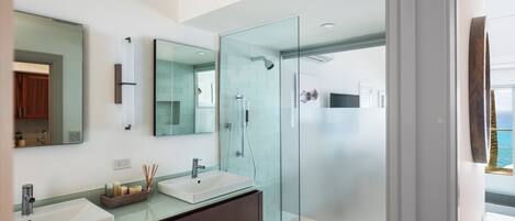 Un baño moderno con dos lavamanos, cabina de ducha de vidrio y un espejo grande.