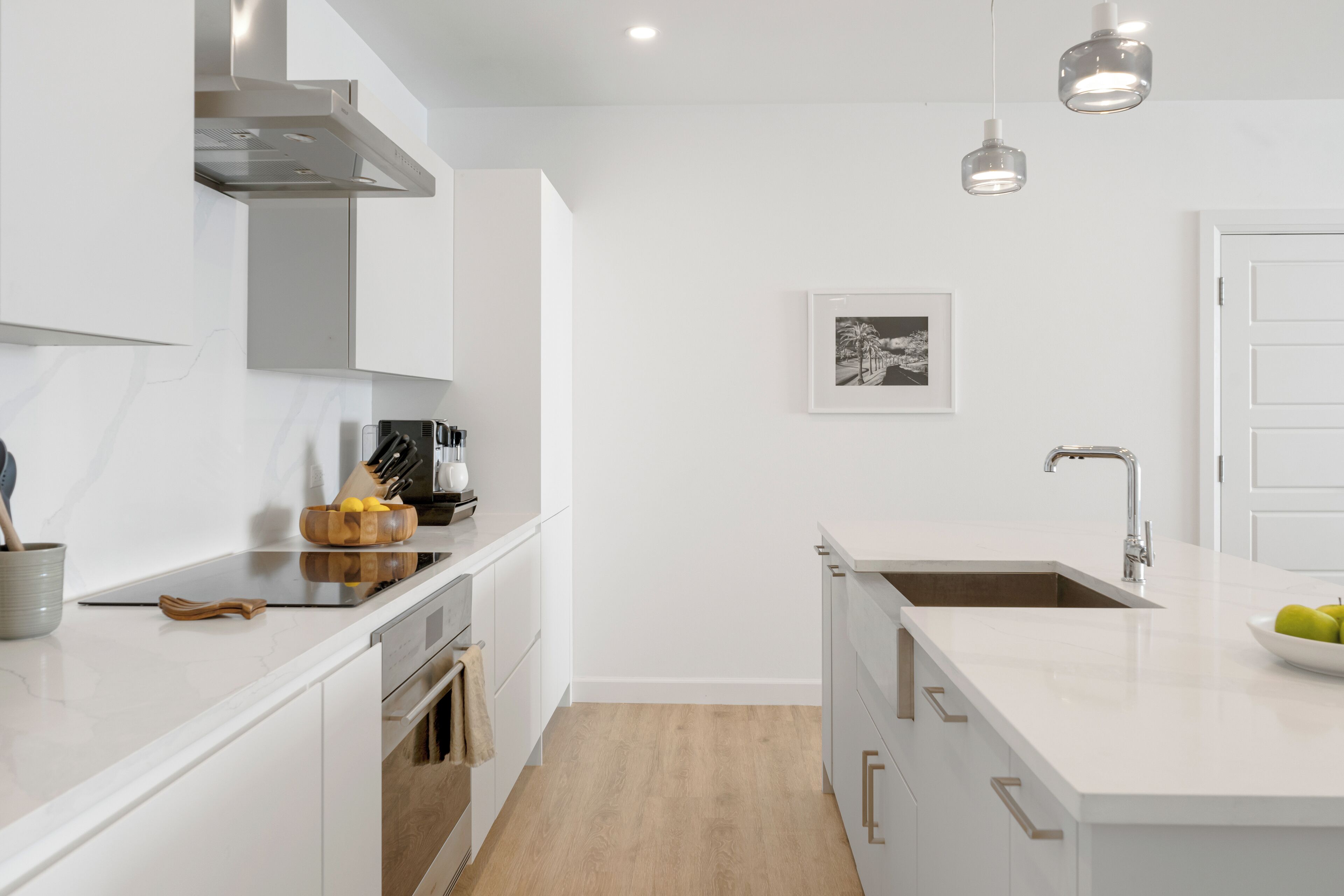 A modern kitchen with white cabinetry, a stainless steel range hood, a double sink, and pendant lighting.