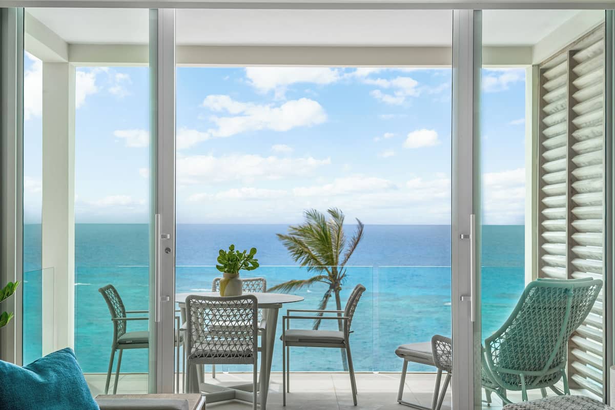 Uma varanda com vista para o oceano, uma mesa com cadeiras e um vaso com planta.
