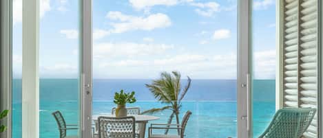 A balcony with a view of the ocean, a table with chairs, and a potted plant.
