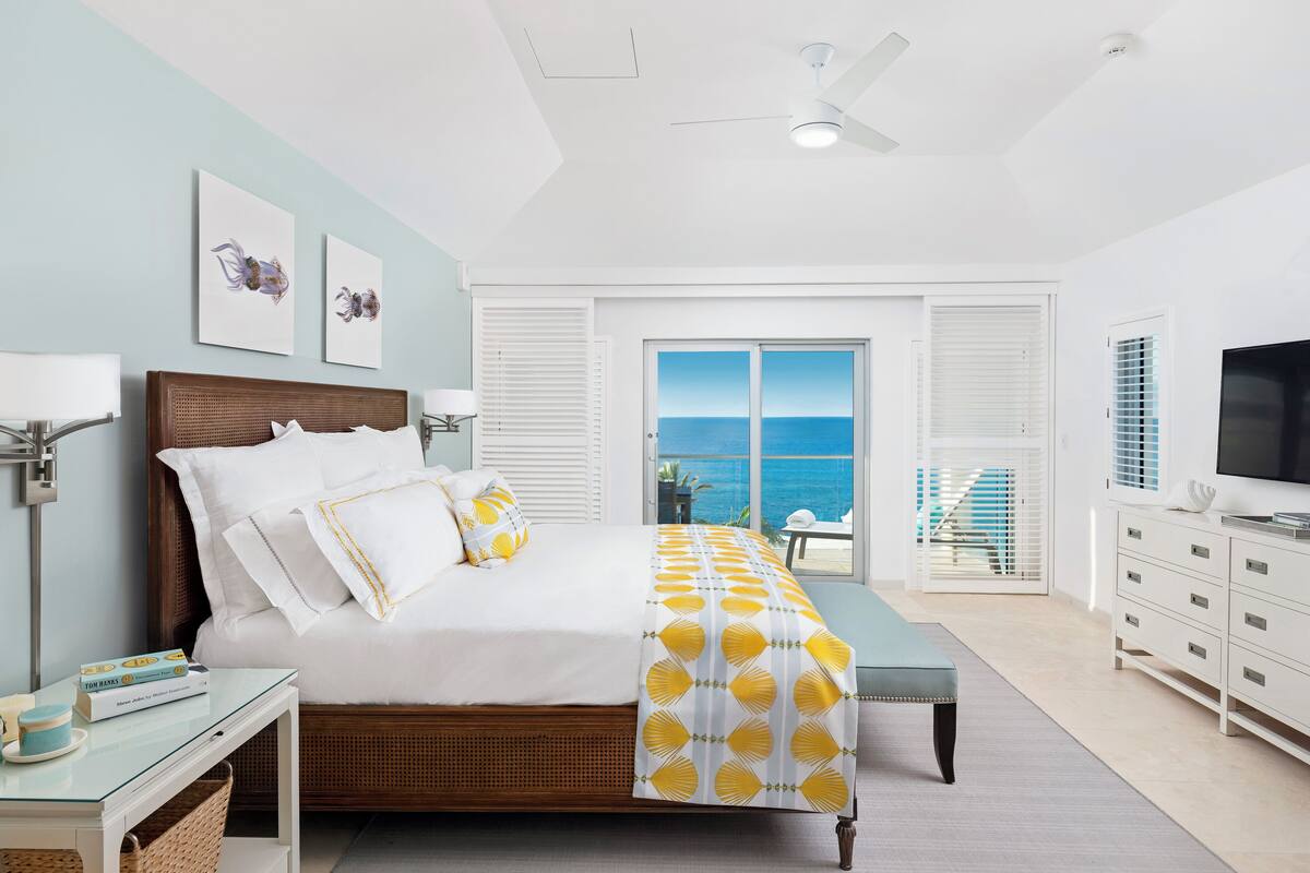 Quarto moderno com cama, mesa de cabeceira e vista para o oceano.