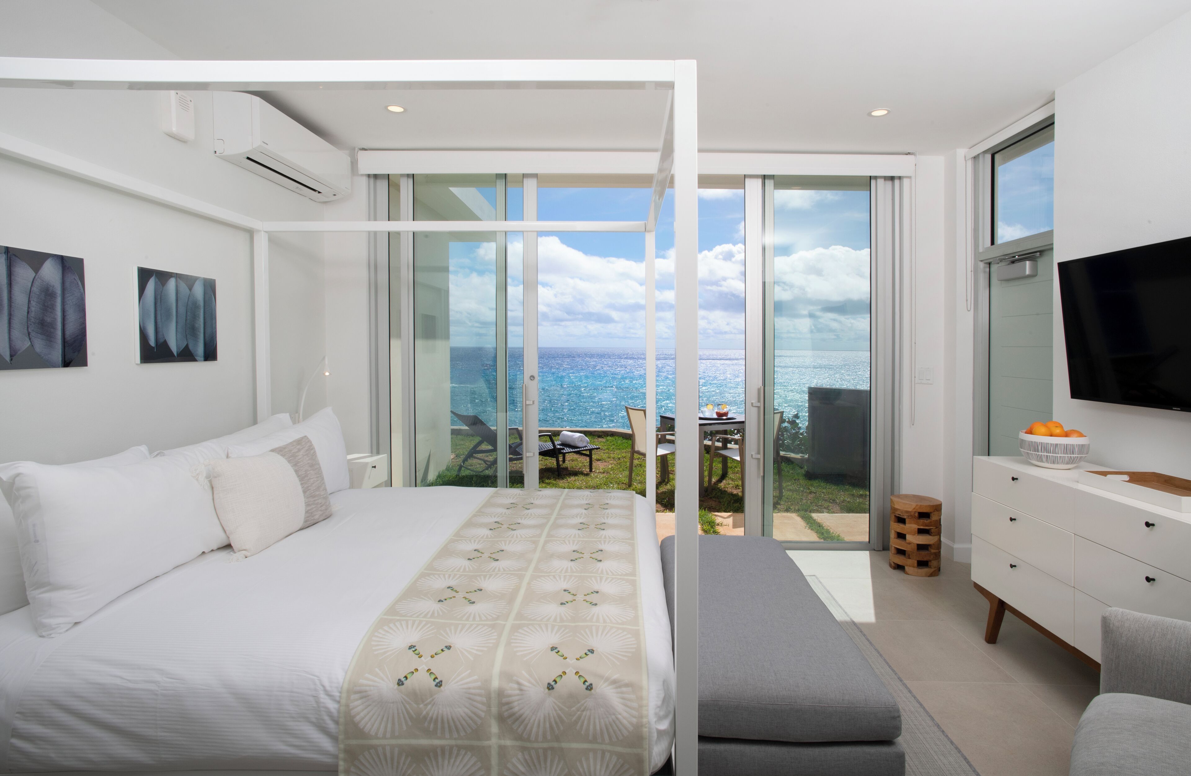 Un dormitorio moderno con una cama grande, un televisor y un balcón con vista al océano.