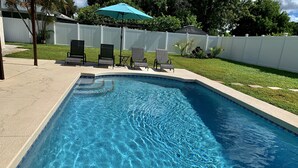A rectangular swimming pool with clear blue water, surrounded by a white fence and a grassy area. - Home with private heated pool (Bradenton)
