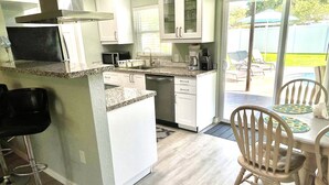 A modern kitchen with white cabinets, a granite countertop, and a dining area with wooden chairs and a table. - Home with private heated pool (Bradenton)