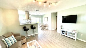 A modern living room with a sofa, a coffee table, a TV, and a dining area with chairs and a table. - Home with private heated pool (Bradenton)