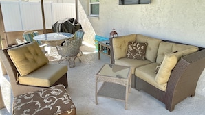 An outdoor patio with wicker furniture, a glass table, and a cushioned bench. - Home with private heated pool (Bradenton)