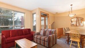 A living room with a red sofa, striped armchair, wooden coffee table, and a dining area with a wooden table and chairs.