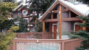 A wooden cabin with a pool, surrounded by trees.