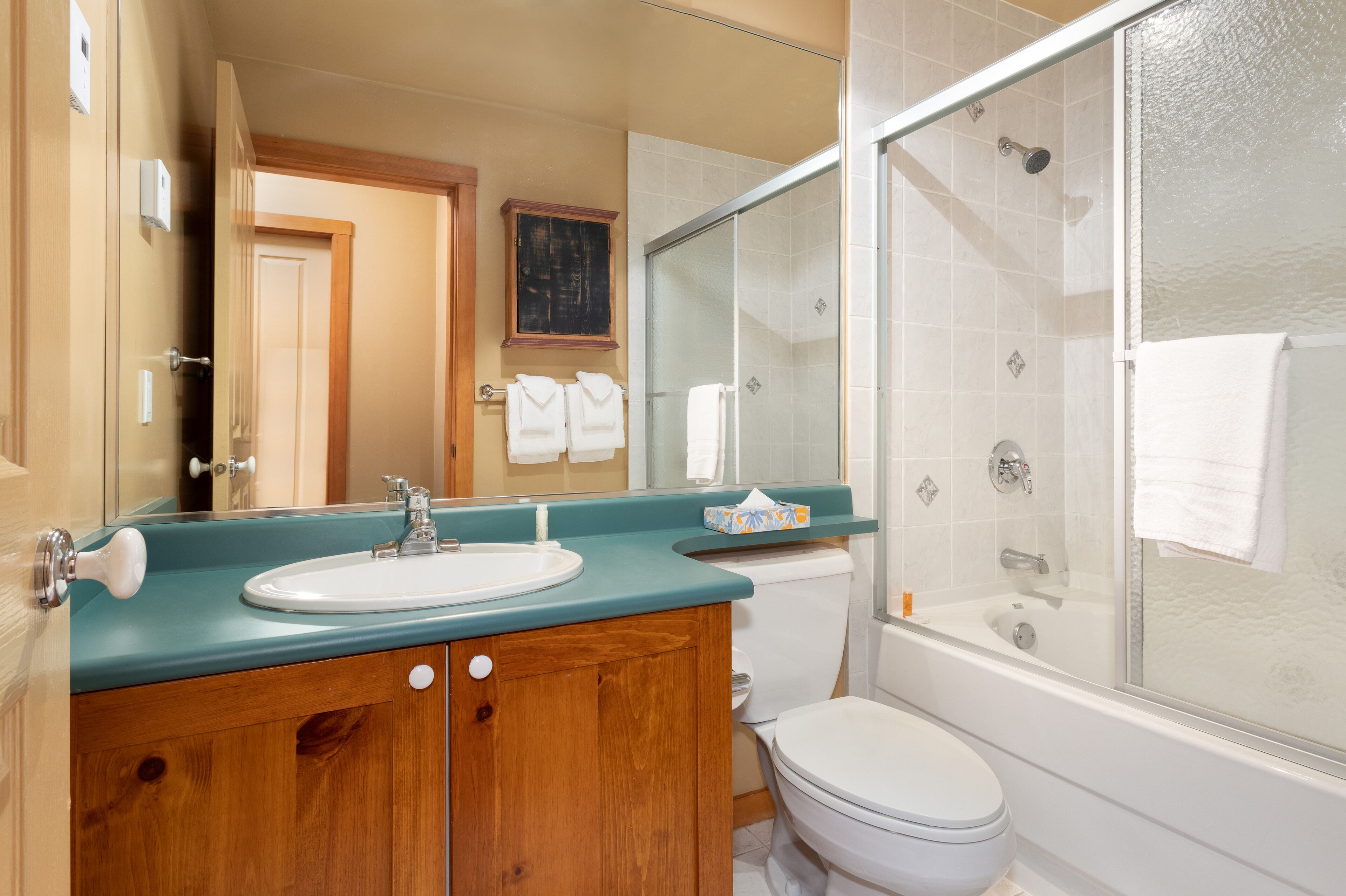 Une salle de bain avec un meuble-lavabo en bois, un lavabo blanc, une cabine de douche en verre et des toilettes blanches.