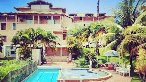 A swimming pool with two lanes, surrounded by palm trees and a building with multiple balconies. - Pousada Herva Doce (Rio das Ostras)